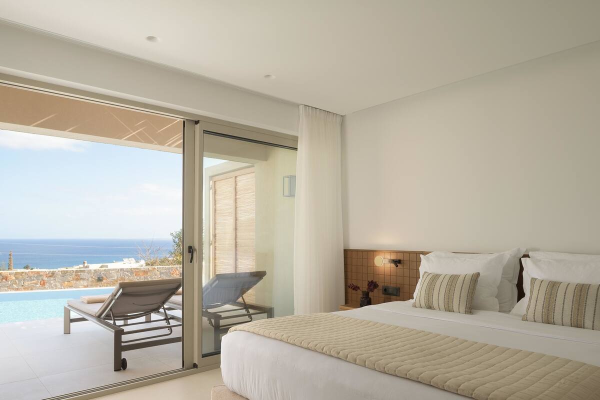 A modern hotel room with a large bed, a view of the sea, and a balcony with a chair.