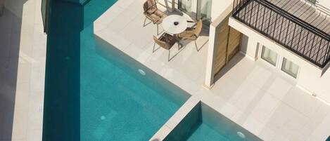 Una piscina en la azotea con barandilla de cristal, una mesa con sillas y vistas del exterior del edificio.