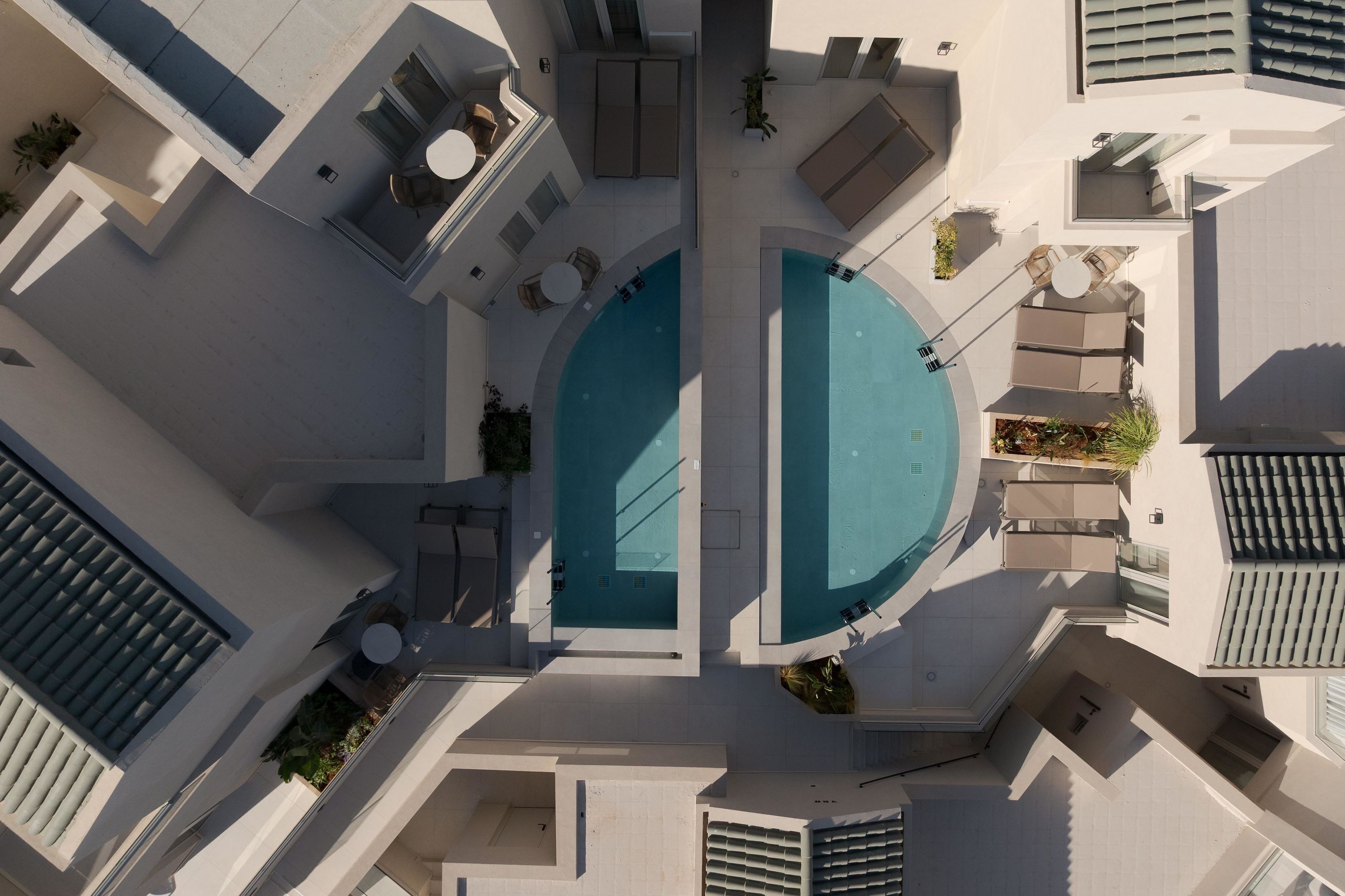 Vista aérea de un hotel moderno con dos piscinas, zonas de estar al aire libre y una terraza en la azotea.