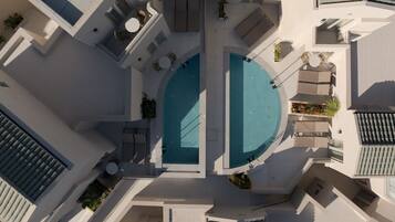 Vista aérea de un hotel moderno con dos piscinas, zonas de estar al aire libre y una terraza en la azotea.