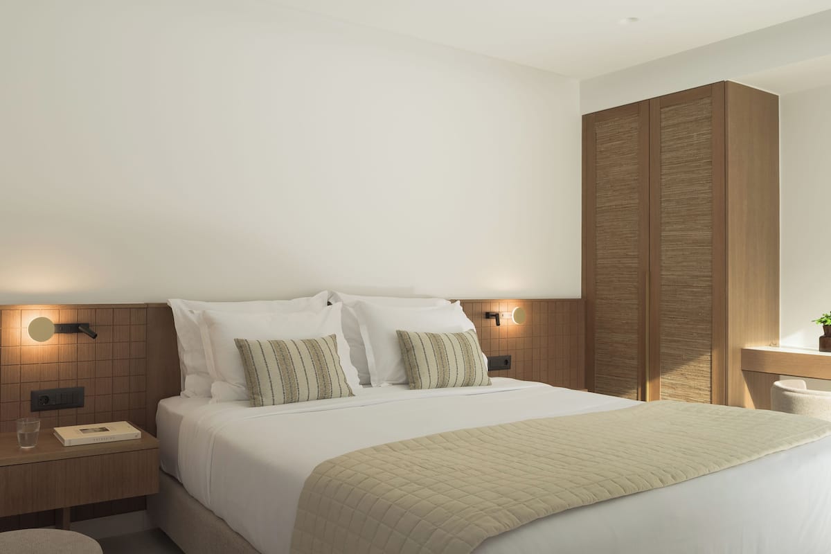 A modern hotel room with a large bed, two bedside tables, a nightstand, a bedside lamp, and a wooden wardrobe.
