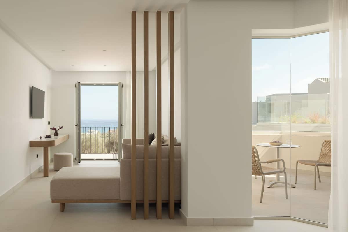 A modern bedroom with a balcony, a sofa, a small table, and a TV mounted on the wall.