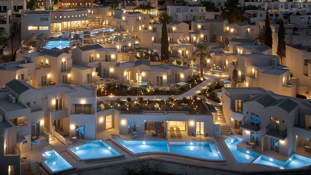Un hotel moderno con varias piscinas, zonas de estar al aire libre y balcones bien iluminados.