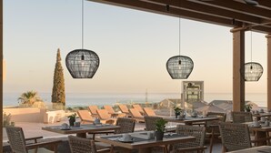 Un restaurante frente al mar con terraza, sillas de mimbre e iluminación colgante.