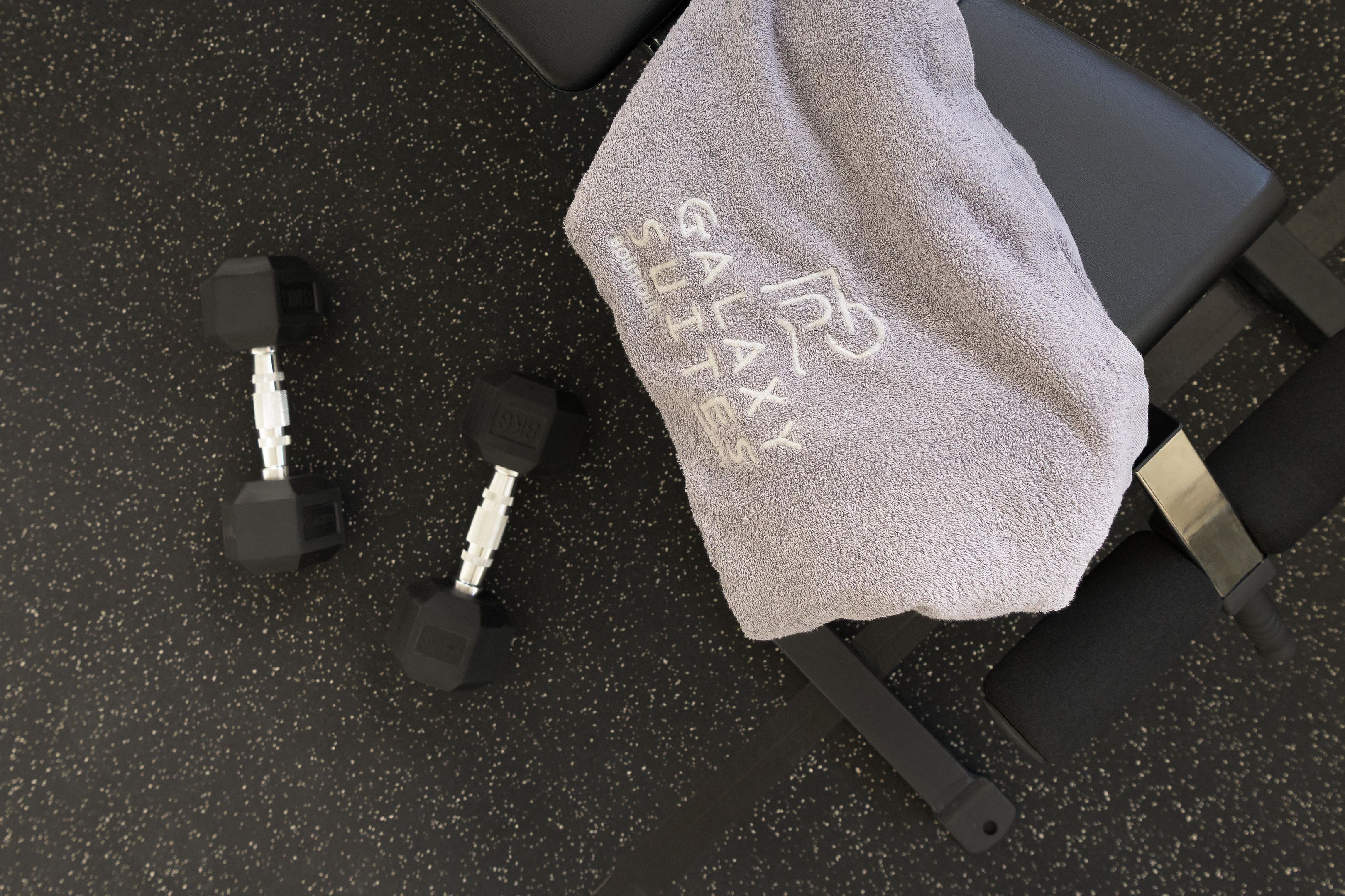 Un gimnasio con suelo negro, una toalla y dos mancuernas.