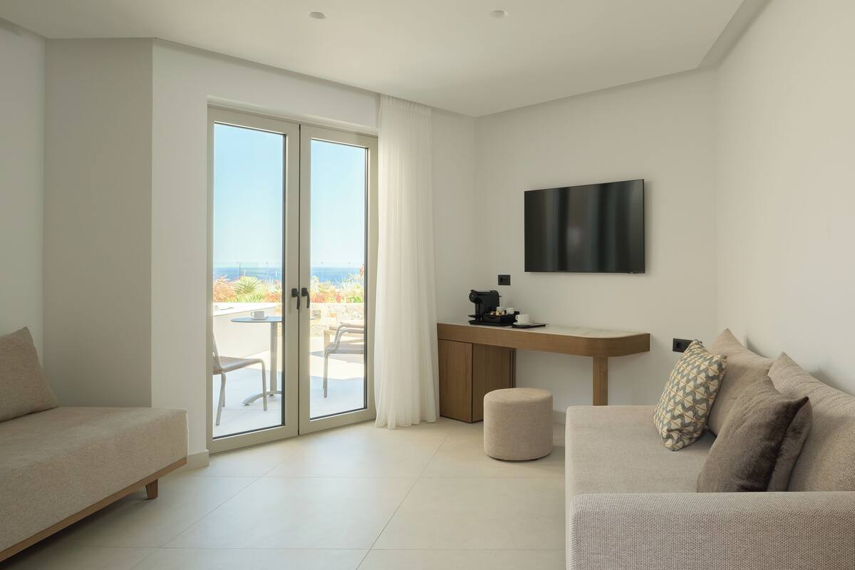 A modern living room with a sofa, a coffee table, a desk with a coffee maker, and a TV mounted on the wall.