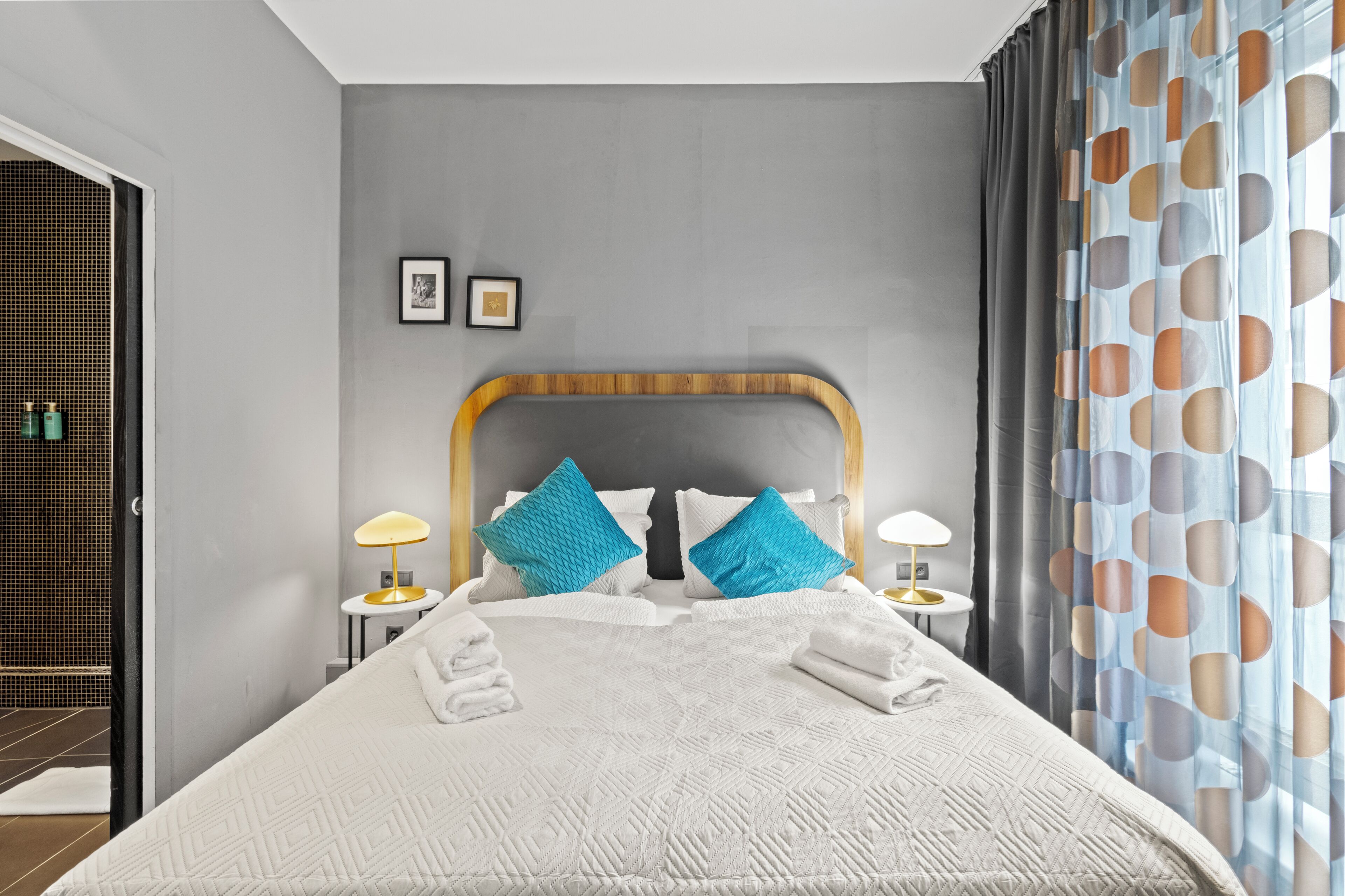 Una cama bien hecha con una colcha de estampado geométrico, dos almohadas azules y dos lámparas de noche.