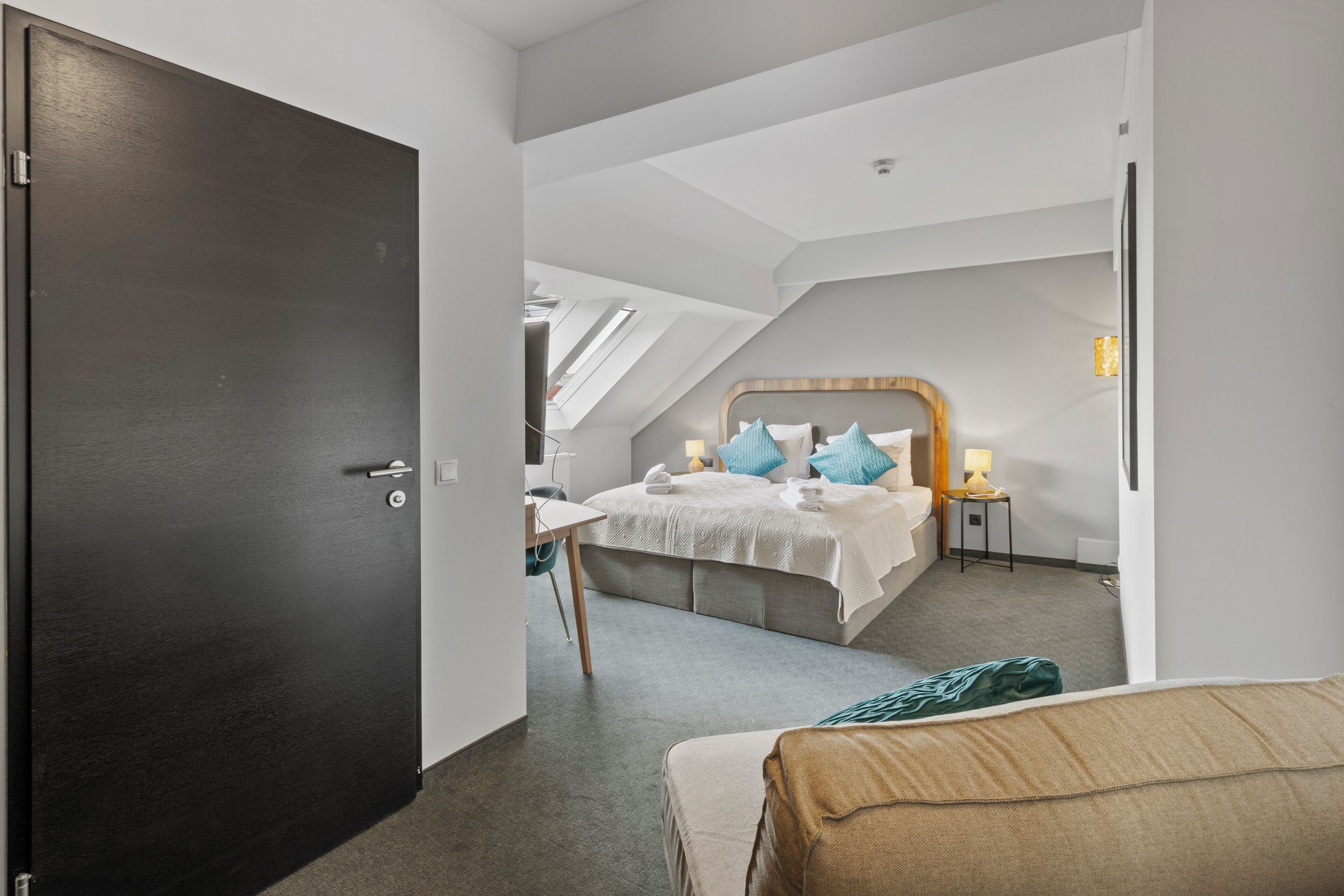 A modern hotel room with a large bed, a desk, and a chair.