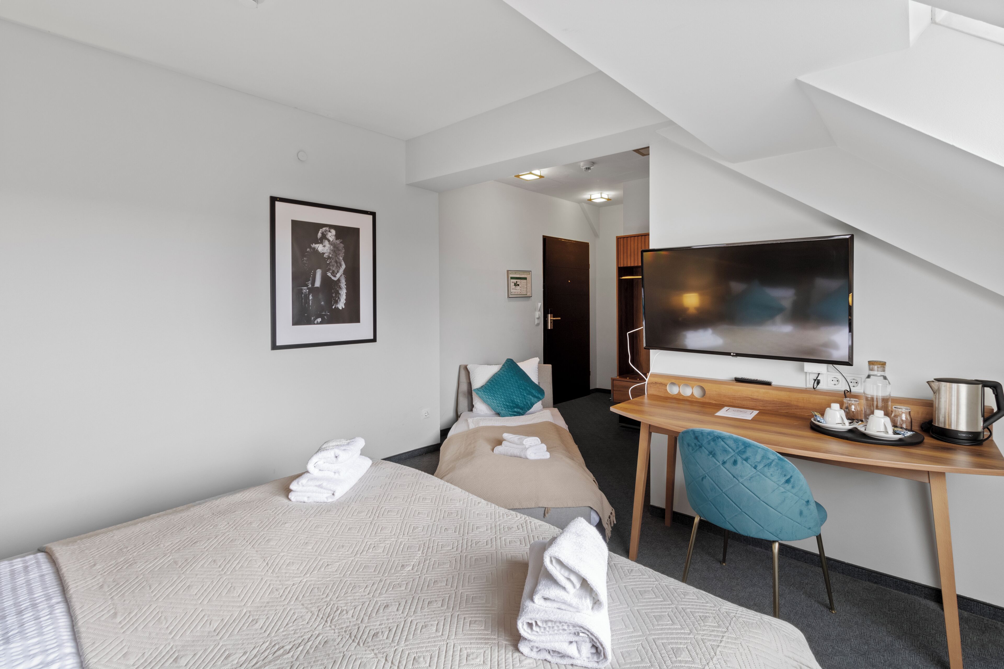 Habitación de hotel con dos camas, un escritorio con silla, televisión y kitchenette.