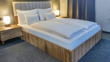 A neatly made bed with a wooden frame and a headboard, accompanied by two bedside tables with lamps, in a room with a carpeted floor.