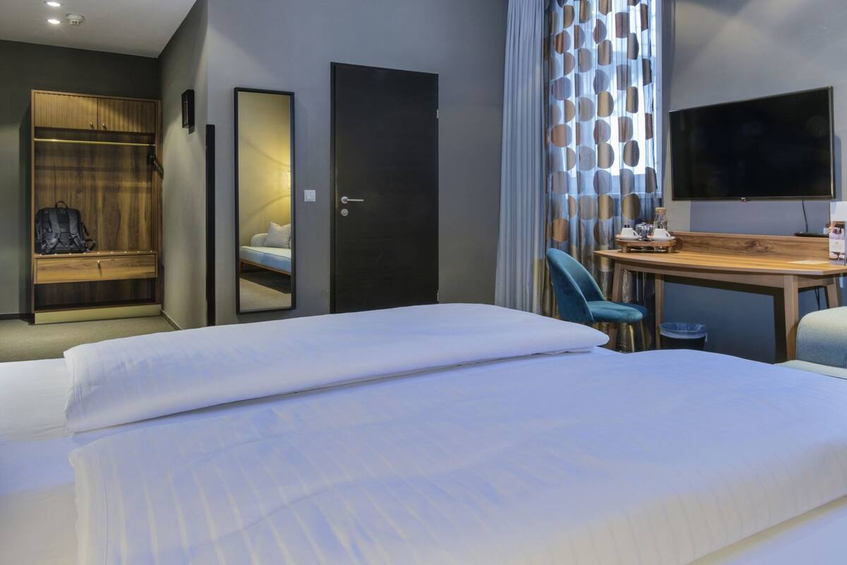 A hotel room with a bed, a desk, a chair, a wardrobe, a mirror, and a television.
