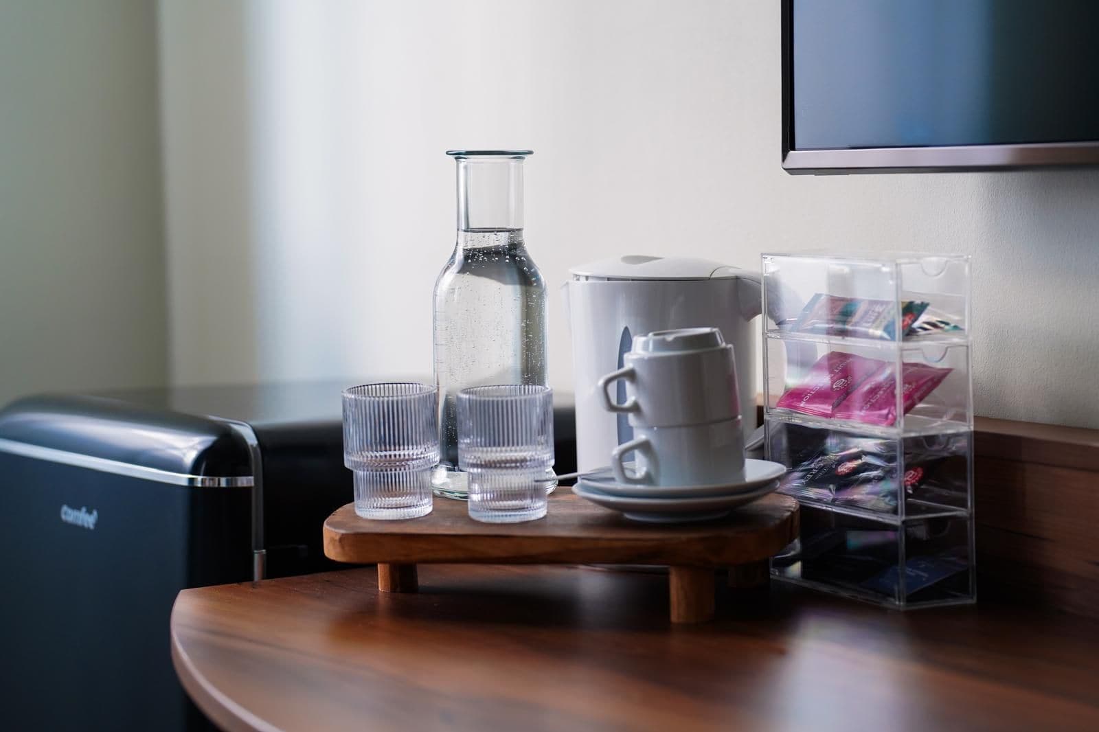 Une petite table avec une machine à café, une bouteille d’eau et deux verres.