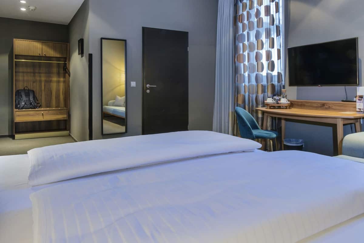 A hotel room with a bed, a desk, a chair, a wardrobe, a mirror, and a television.