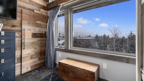 Ein Zimmer mit einer Holzwand, einem großen Fenster mit Blick auf eine verschneite Landschaft, einer Bank und einem dunklen Schrank.
