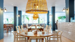 Een ruime eetruimte met meerdere tafels en stoelen, een hanglamp in het midden en uitzicht op het buitenland.