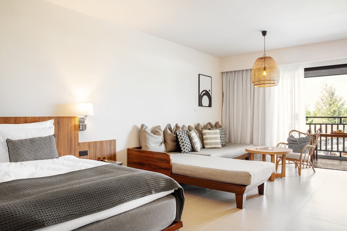 Habitación de hotel con dos camas, un sofá, una mesa de comedor y un balcón con vistas.