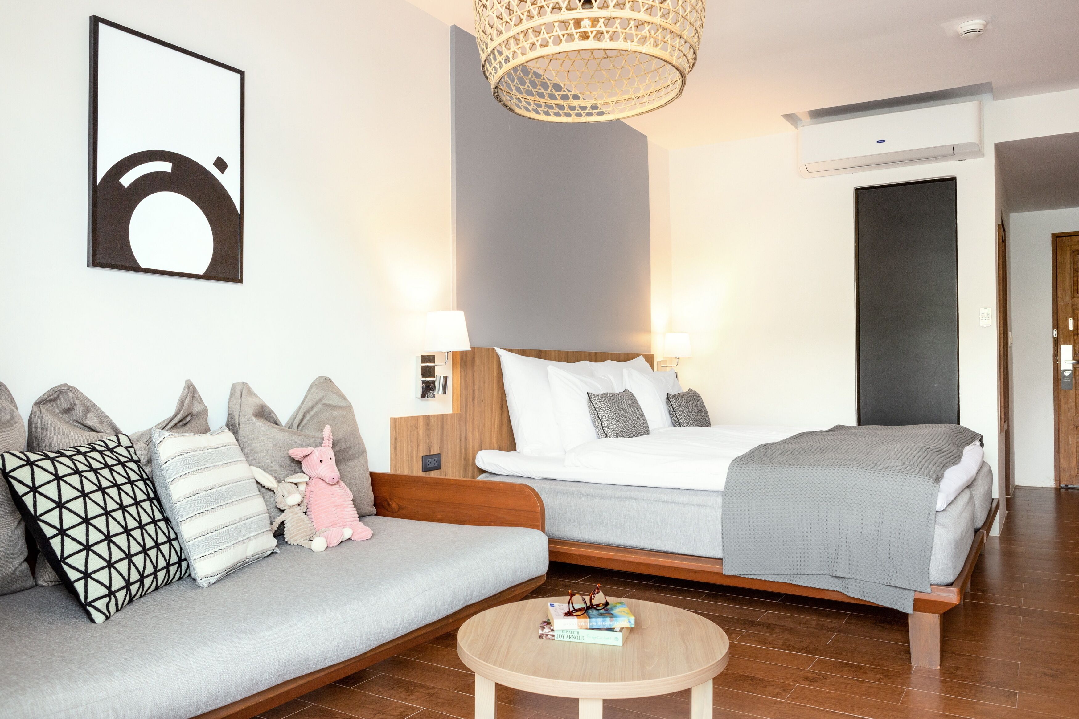 A modern hotel room with a sofa, two beds, a round coffee table, and a hanging light fixture.