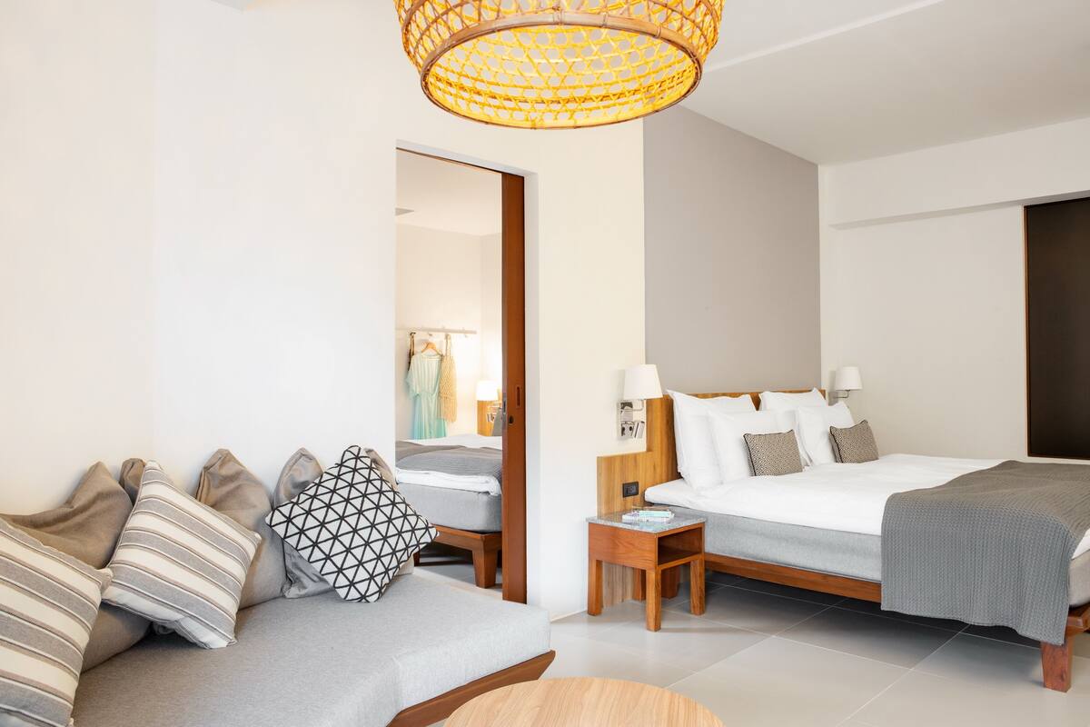 Una habitación de hotel moderna con una cama grande, un sofá, una mesita de noche y un espejo.