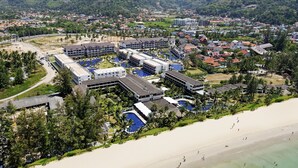 Een luchtendruk van een resort met meerdere gebouwen, een strand en omliggende begroeiing.