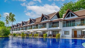 Een modern hotel met een groot zwembad, meerdere balkons en buitenzitplaatsen.