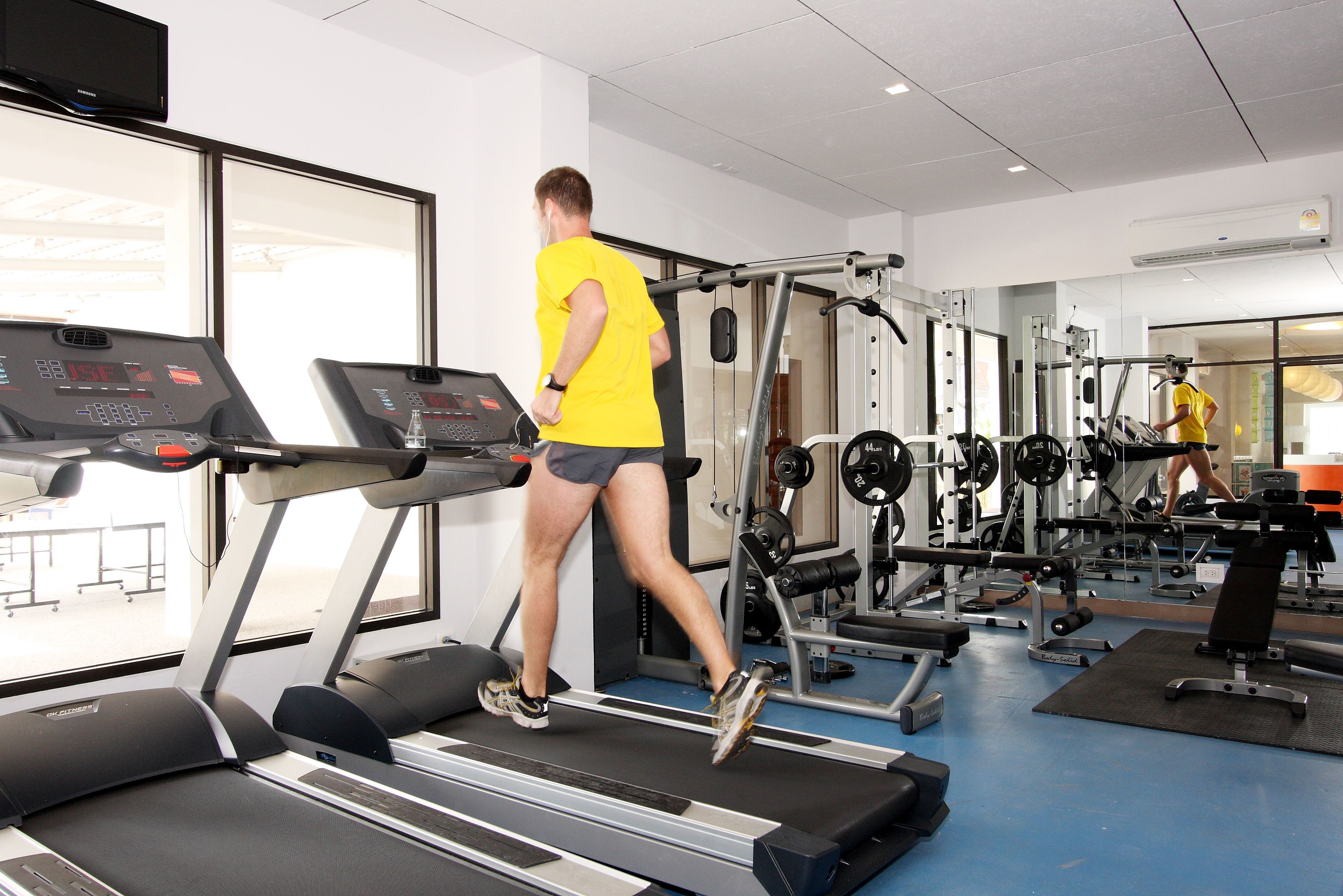 Une salle de sport équipée de tapis de course, d’appareils de musculation et d’un grand miroir.