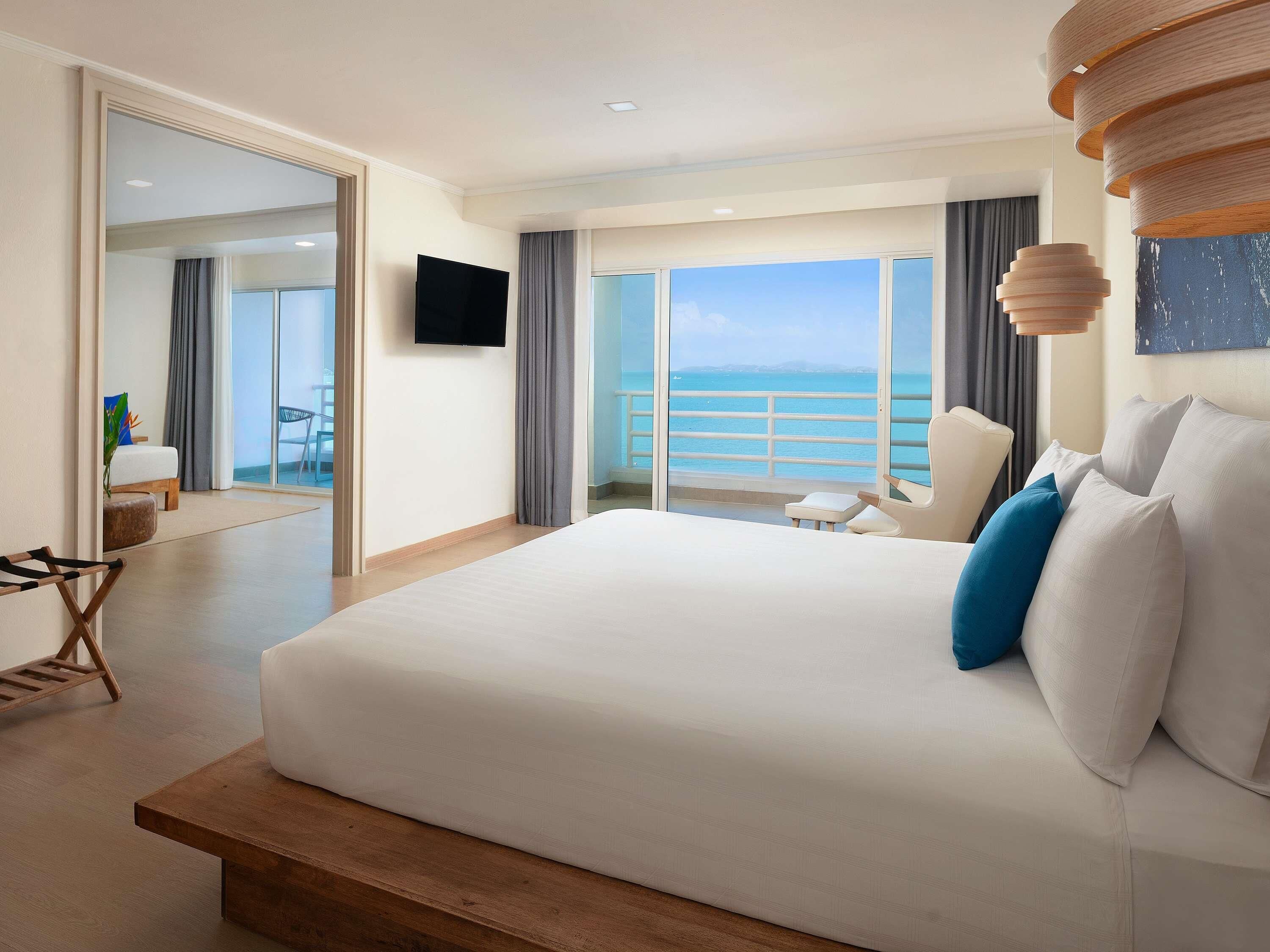 Habitación de hotel con una cama grande, televisión, vistas al mar y un balcón.