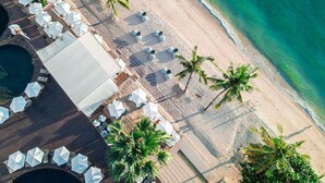 Vista aerea di un resort sulla spiaggia, con file di ombrelloni bianchi, lettini da relax e palme.