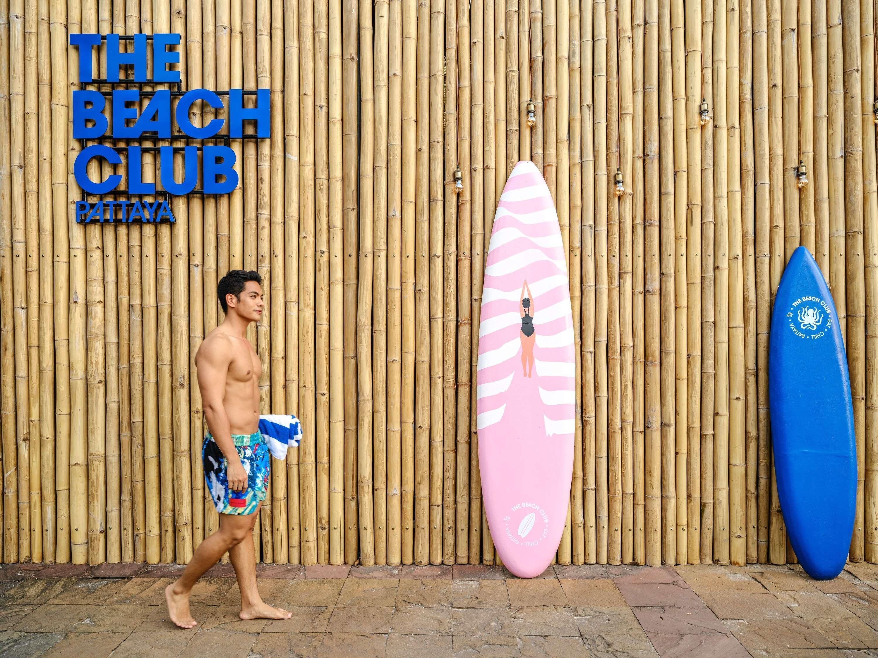 Un homme passe devant un mur de bambou sur lequel est affiché un panneau indiquant : « The Beach Club Pattaya ».