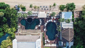 Vista aerea di un resort con un'ampia area piscina, accesso alla spiaggia e palme.