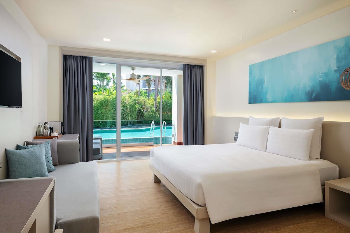A hotel room with a large bed, a desk, and a view of a swimming pool.