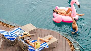 A poolside area with lounge chairs, a wooden deck, and a pink flamingo float.
