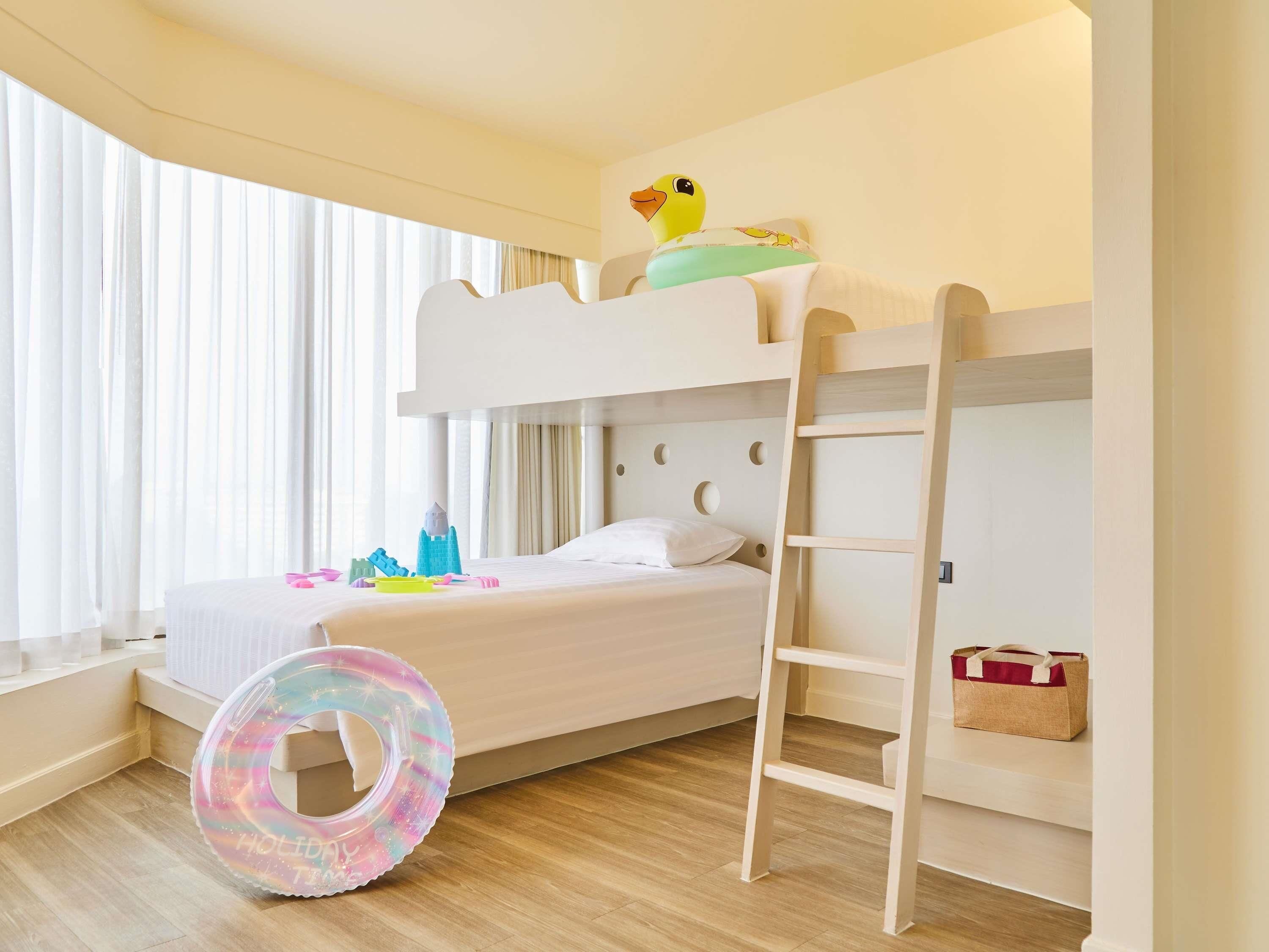 Une chambre avec un lit superposé, une échelle, une fenêtre avec des rideaux et un lit avec des oreillers et des jouets.