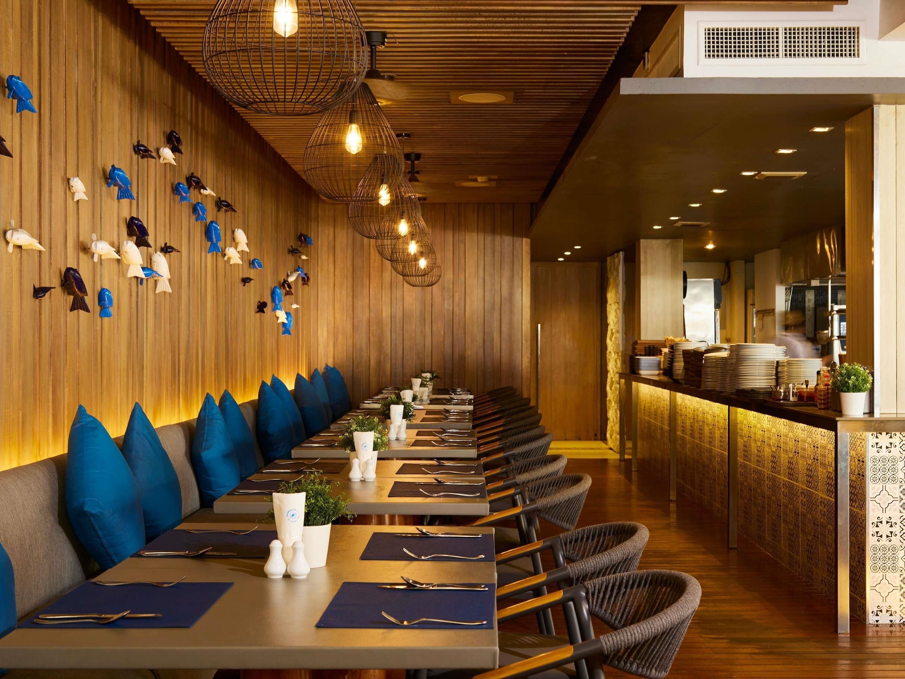 A restaurant with a long counter, blue cushioned seating, and decorative fish wall art.
