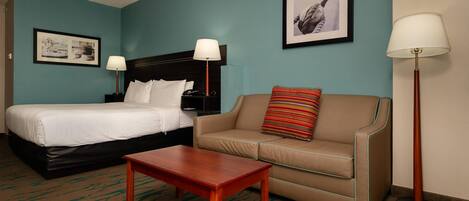 Una habitación de hotel con cama, sofá, una mesita y dos lámparas.