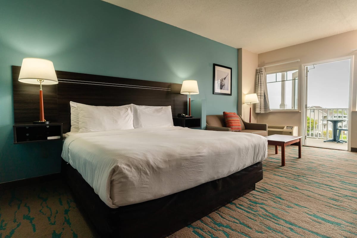 A hotel room with a large bed, two bedside tables with lamps, a chair, a window with a view, and a balcony.