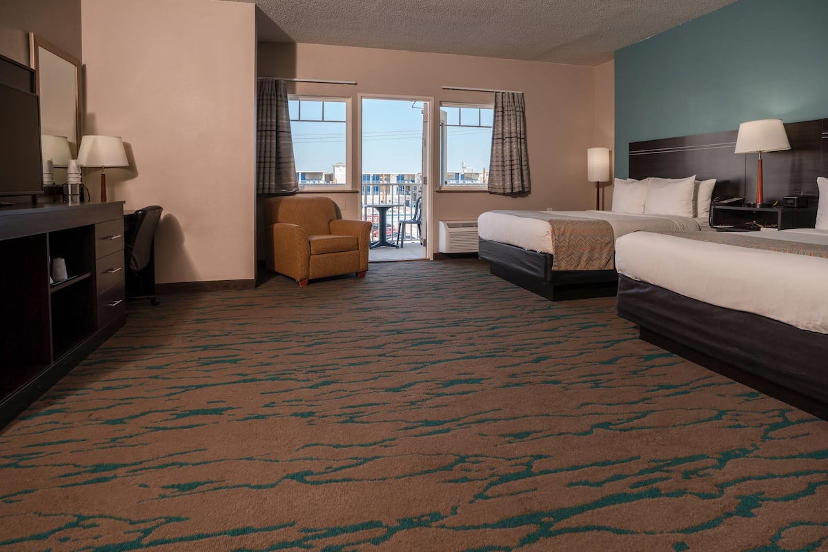 A hotel room with a bed, a desk with a chair, a small table with a chair, and a view of the outside through a door.