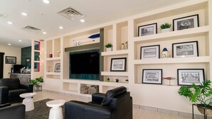 A modern living room with a black leather sofa, white coffee table, and a flat-screen TV mounted on the wall. - Gateway Hotel & Suites Ocean City, an Ascend Collection Hotel (Ocean City)