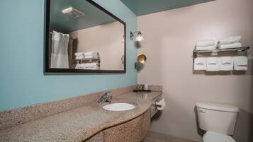 Une salle de bain avec un lavabo doté d’un plan de travail en granit, un miroir, un porte-serviettes et des toilettes.