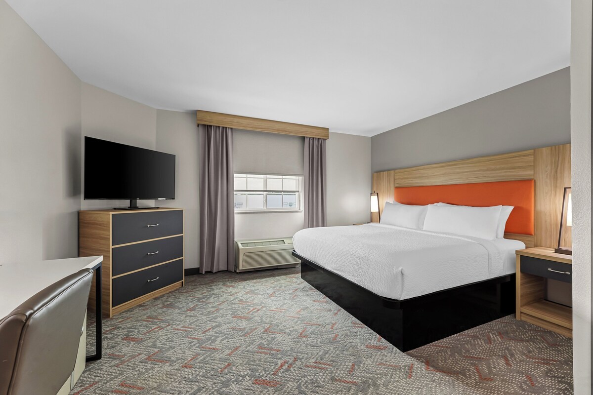 A hotel room with a bed, a TV, a desk, a dresser, and a window with curtains.