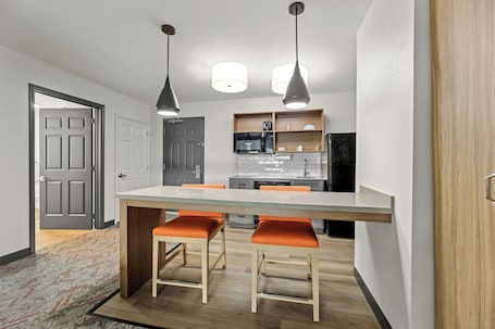 A modern kitchen with a central island, pendant lighting, and a wooden door.
