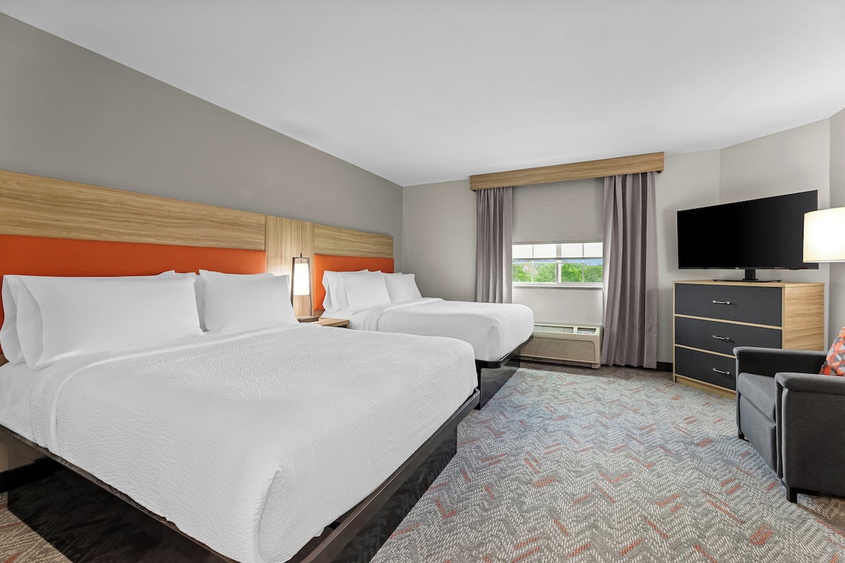 A hotel room with two beds, a TV, a desk, and a window with curtains.