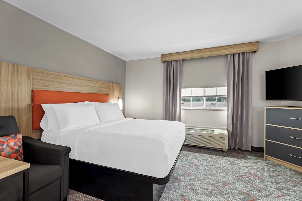 A hotel room with a bed, a desk, a TV, and a window with curtains.