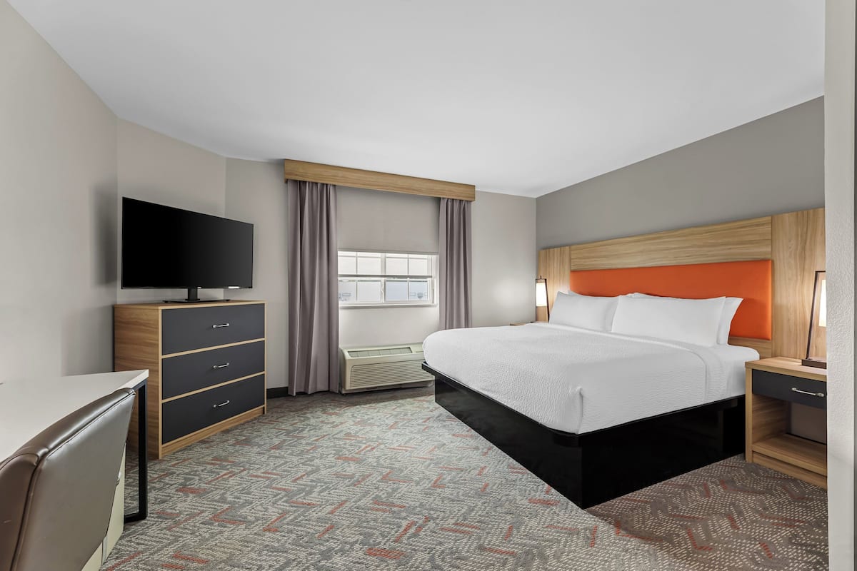 A hotel room with a bed, a TV, a desk, a dresser, and a window with curtains.