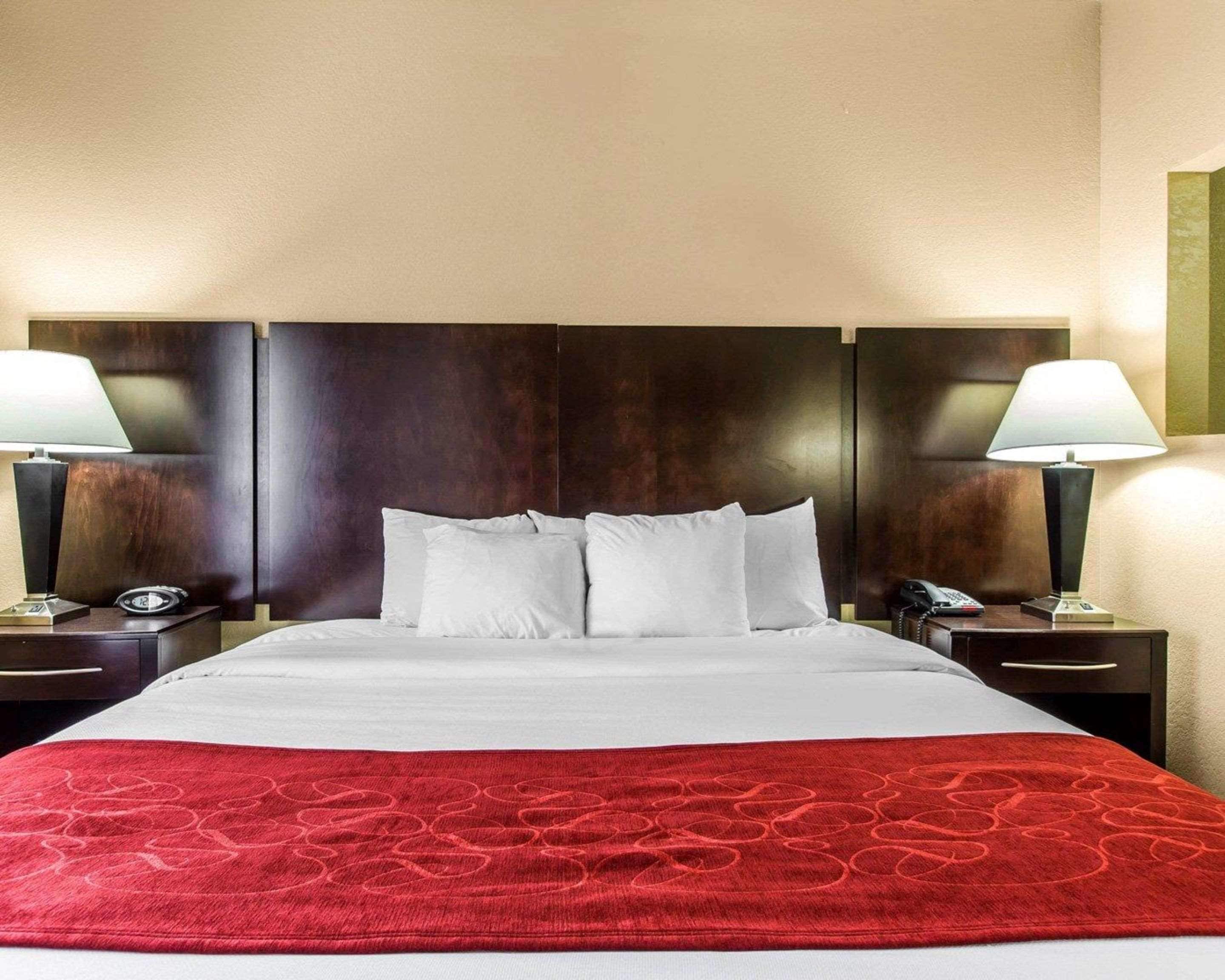 Una habitación de hotel con una cama grande, dos mesitas de noche, una manta roja y dos lámparas.