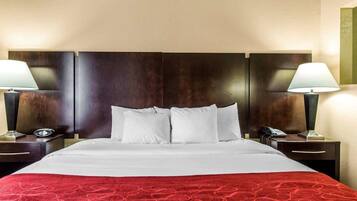 Una habitación de hotel con una cama grande, dos mesitas de noche, una manta roja y dos lámparas.