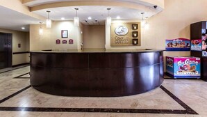 Zona d'entrada d'un hotel amb un taulell de recepció corbat, un cartell que diu 'Comfort Suites' i caixes de gelats De'Conné a la vista.