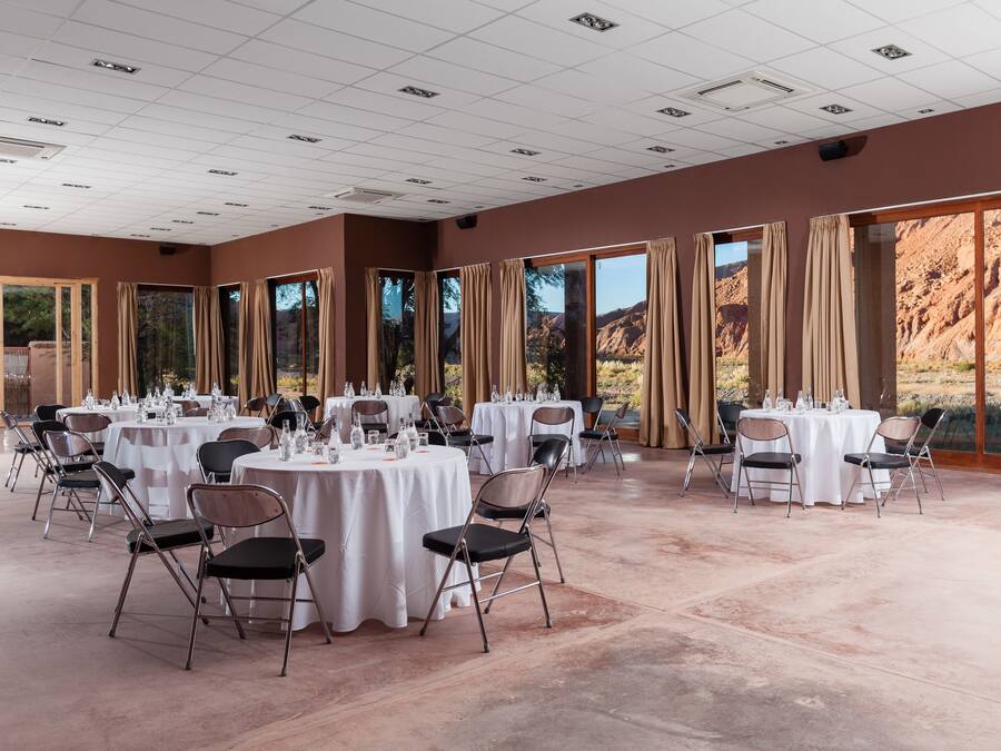 Un vaste espace intérieur doté de plusieurs tables et chaises rondes, de grandes fenêtres avec des rideaux et offrant une vue sur un paysage montagneux.