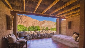 Un patio al aire libre con paredes de piedra, techo de paja y vistas a un paisaje montañoso.