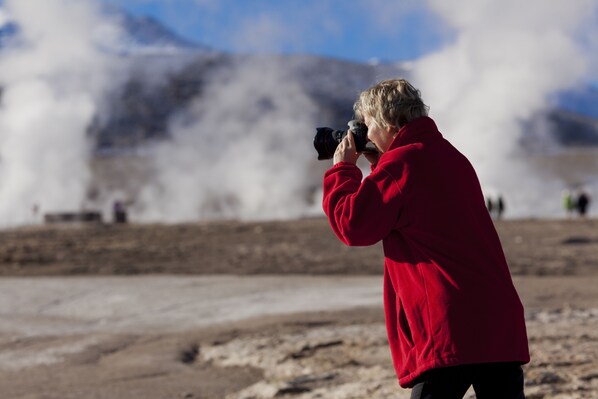 A person in a red jacket taking a photograph with a camera.