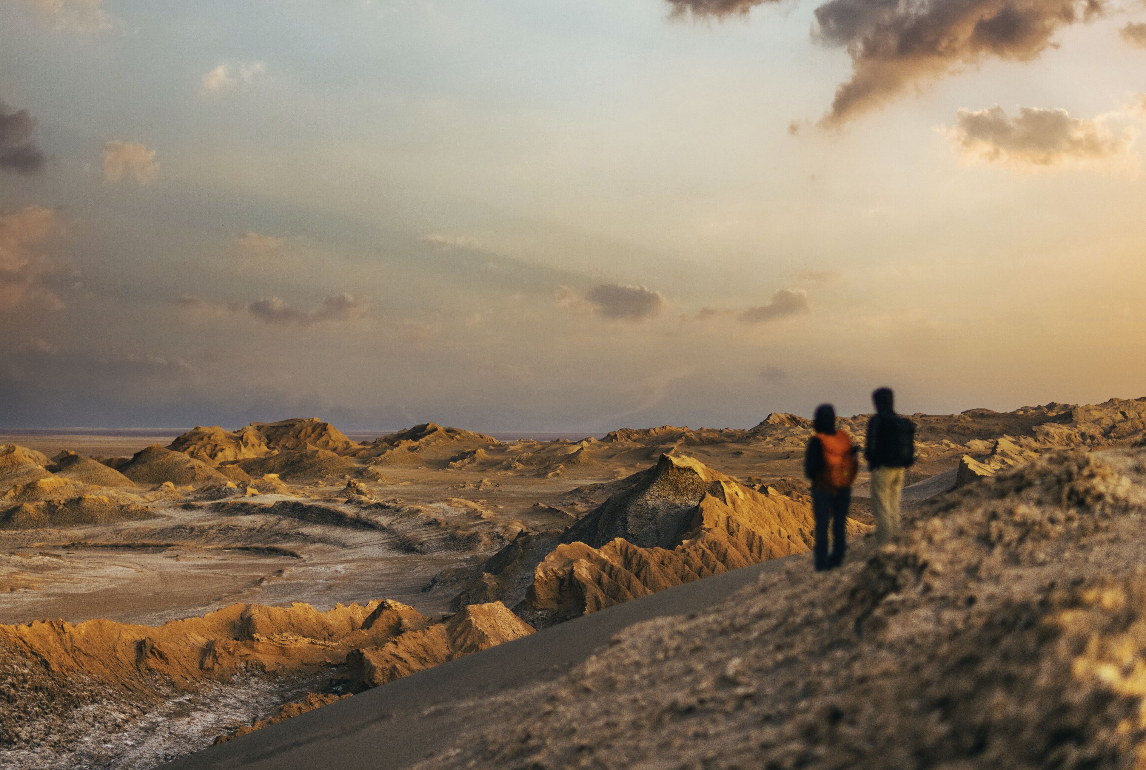 A barren landscape with rocky terrain and two people walking.